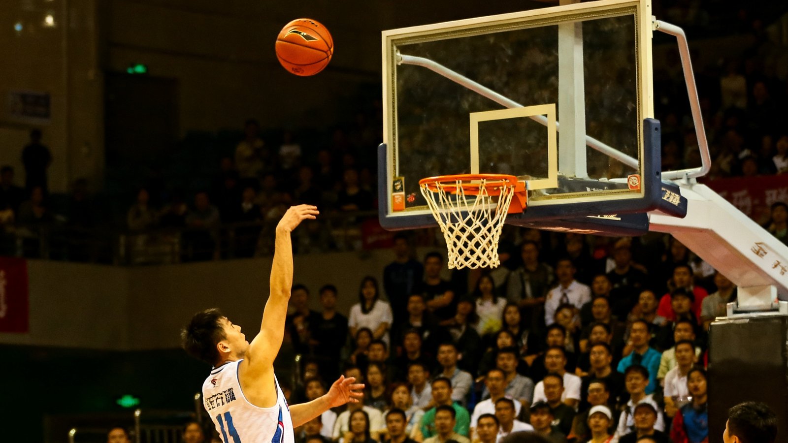 NBA常规赛最后时刻绝杀瞬间的照片，篮球正从三分线外飞向篮筐，出手球员保持投篮跟随动作，全场观众起立屏息注视，计时器显示剩余0.3秒，比分牌上两队分差仅1分